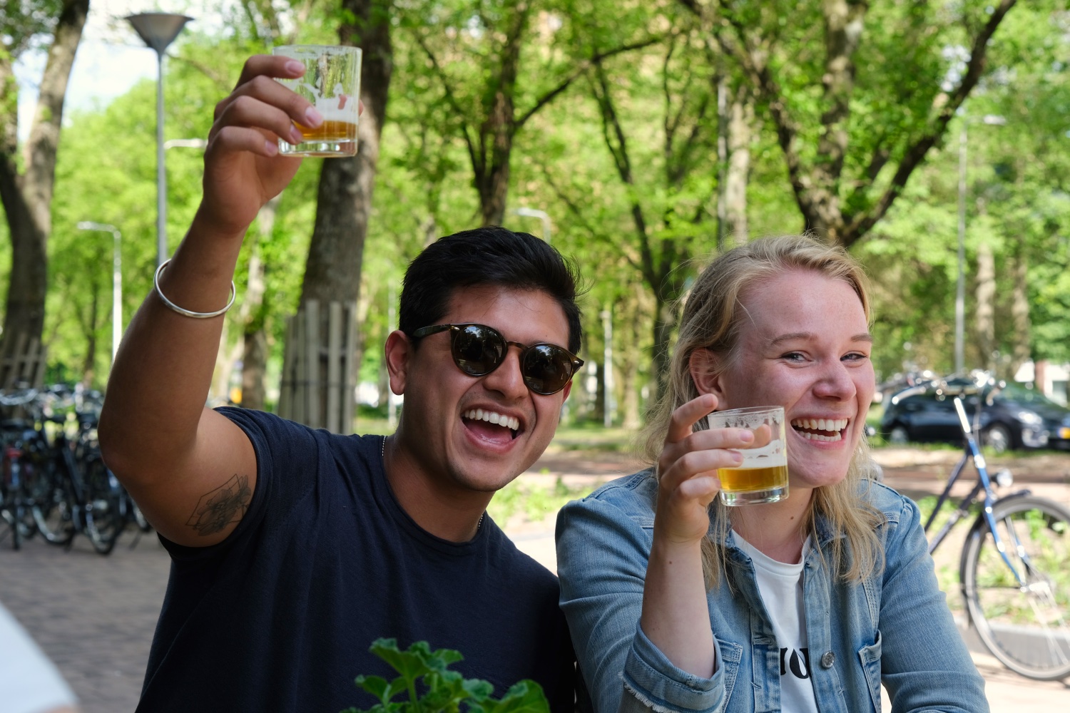 Twee personen zitten buiten met een klein biertje in hun hand - ze proosten