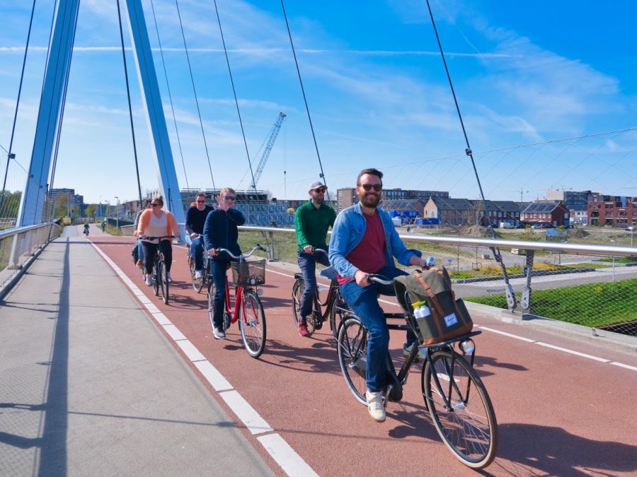 Op een brug met Utrecht op de achtergrond zie je een gids voorop fietsen met een hele stoet aan mensen erachter