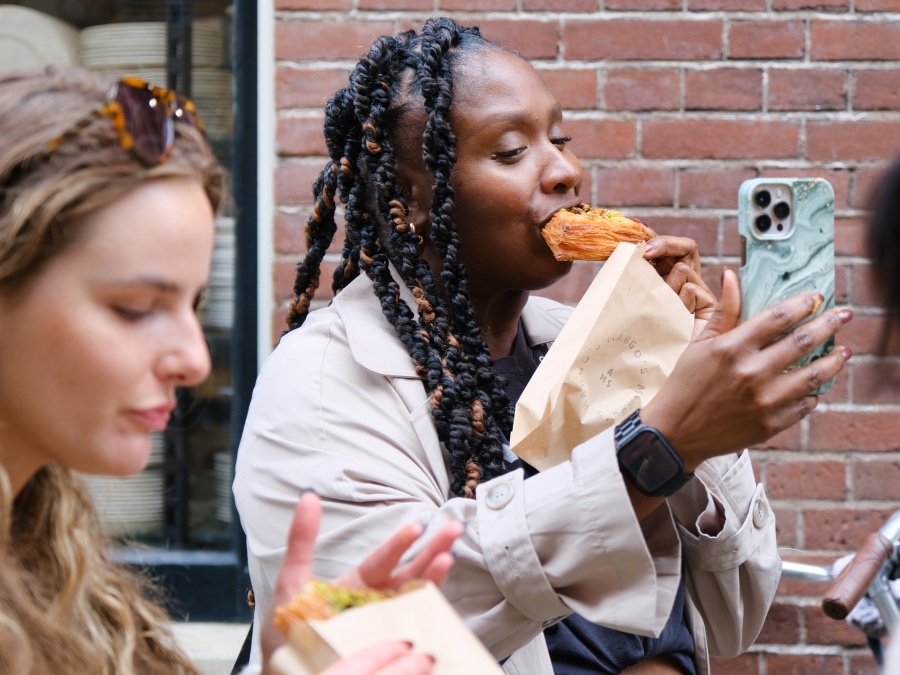 Voor een bakstenen muur zie je een persoon een selfie nemen terwijl ze een hapje neemt van een vienoisserie