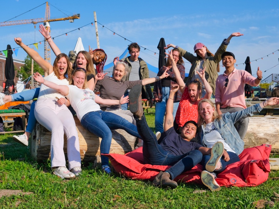 Buiten zie je een groep mensen die allemaal heel blij lachend in de camera kijken