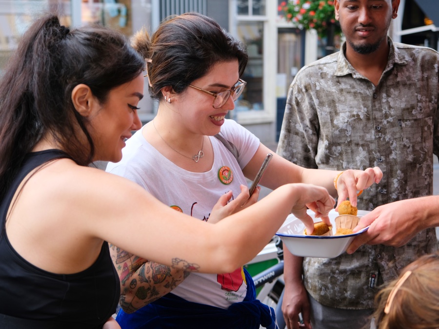 Drie personen staan om een bakje met bitterballen heen. Ze pakken een bitterbal uit het bakje