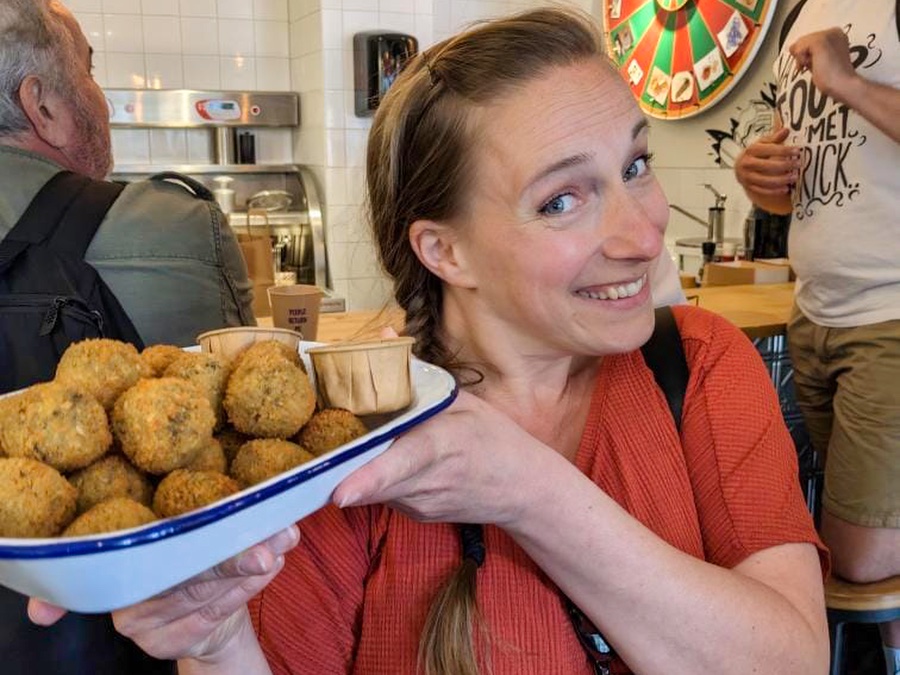 In een vegan snackbar zie je een vrouw heel blij kijken met een hele grote schaal met vegan bitterballen in haar handen