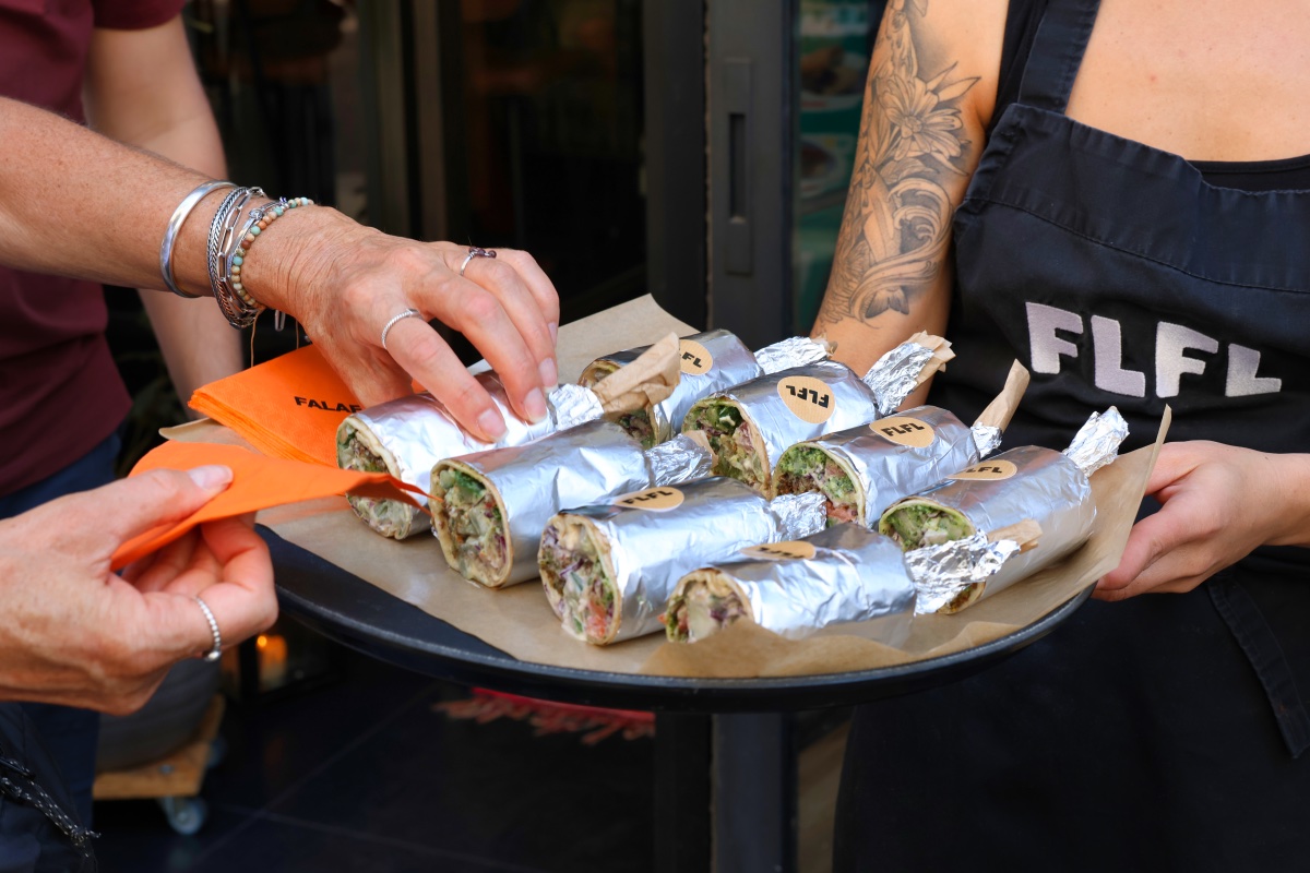 Een dienblad met allemaal wraps met falafel en een hand die er eentje pakt.