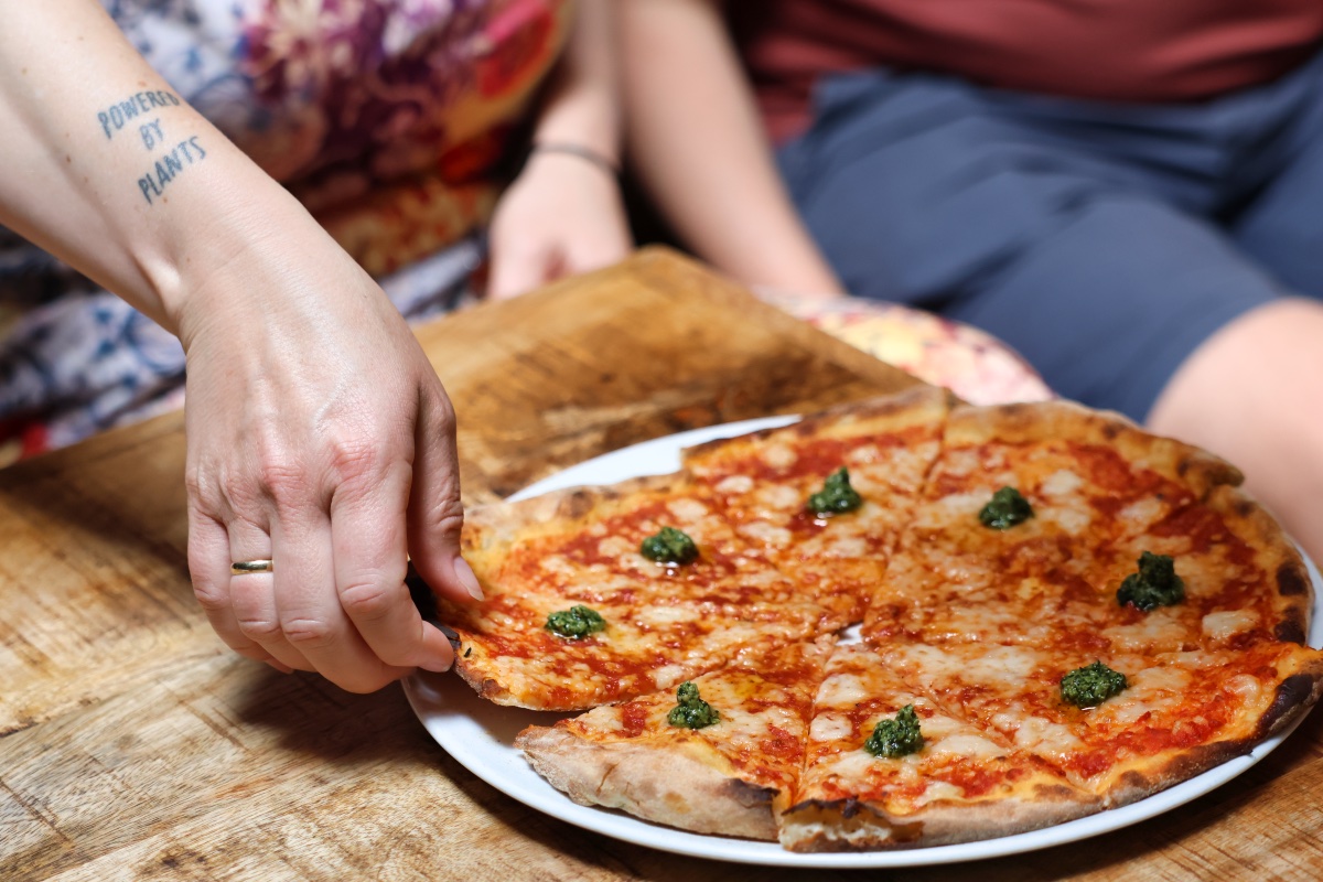 Een arm met een tattoo waarop staat 'powered by plant' die een pizzapunt pakt.
