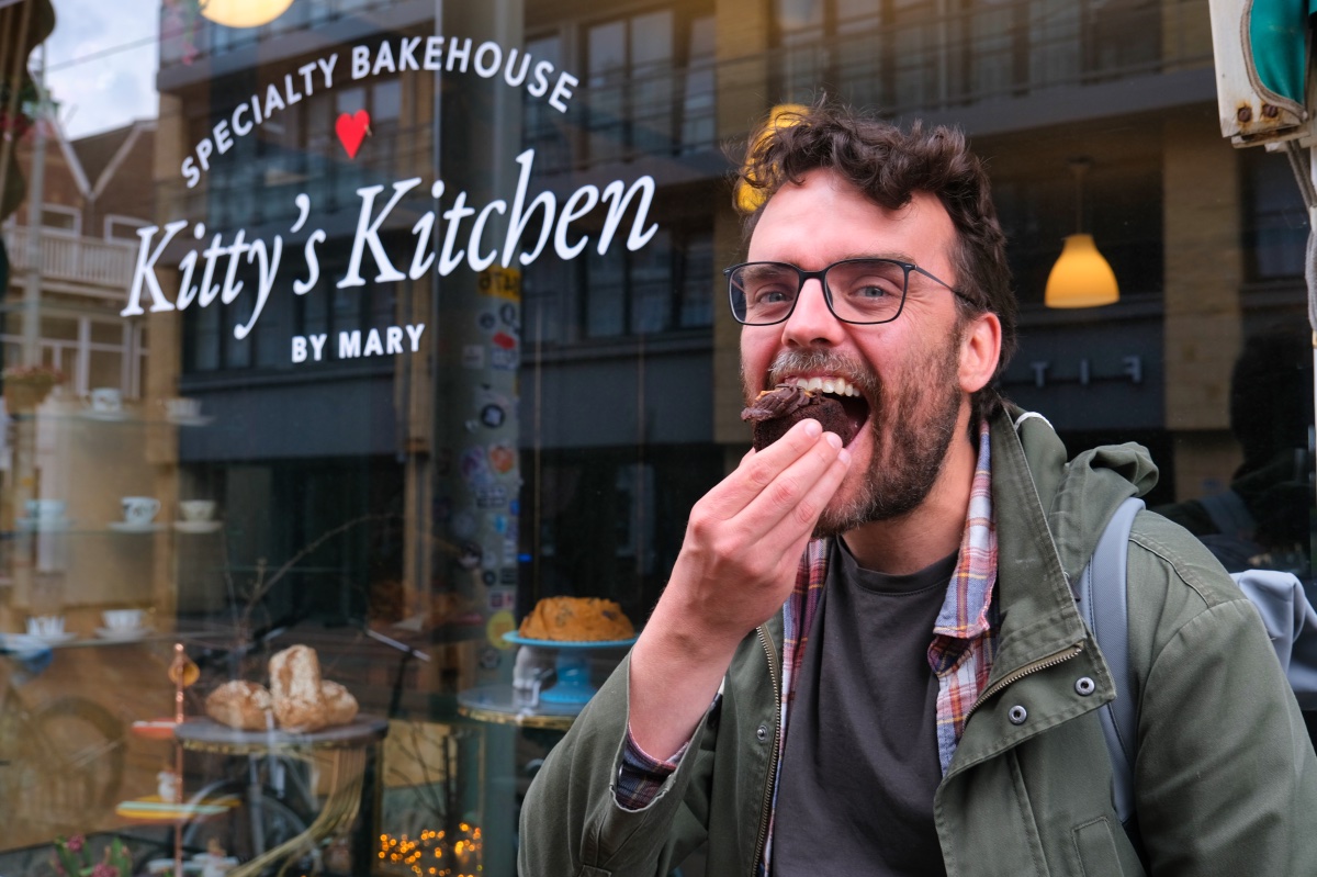 Man neem een hap van een romig chocoladetaartje voor de etalage van een bakkerij tijdens de vegan food tour in Den Haag.